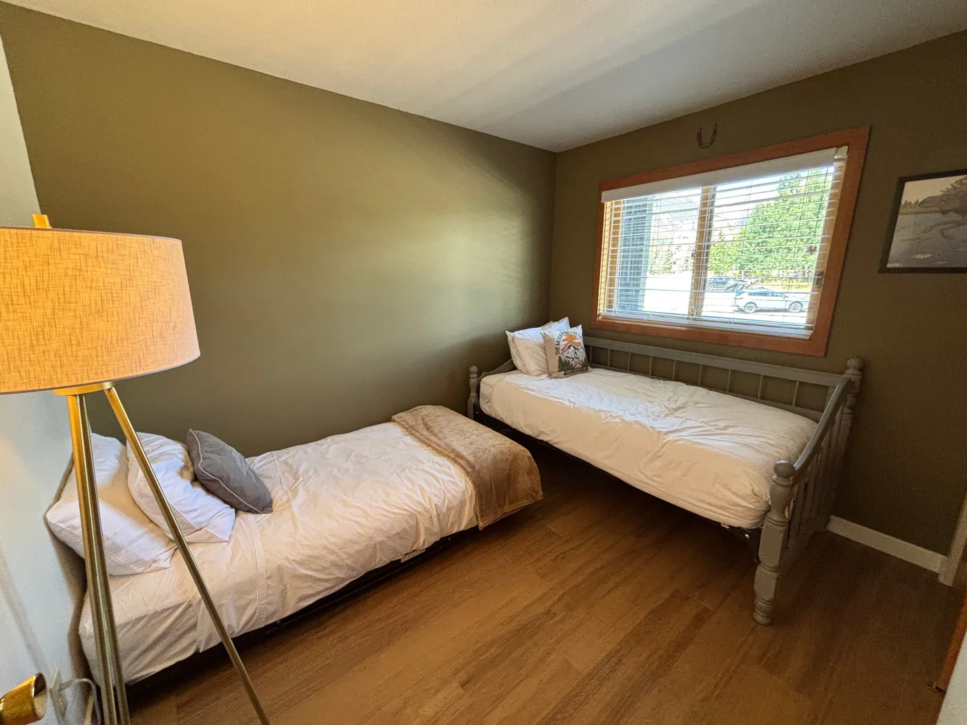 Second bedroom with two single beds, green accent wall, lamp, and window